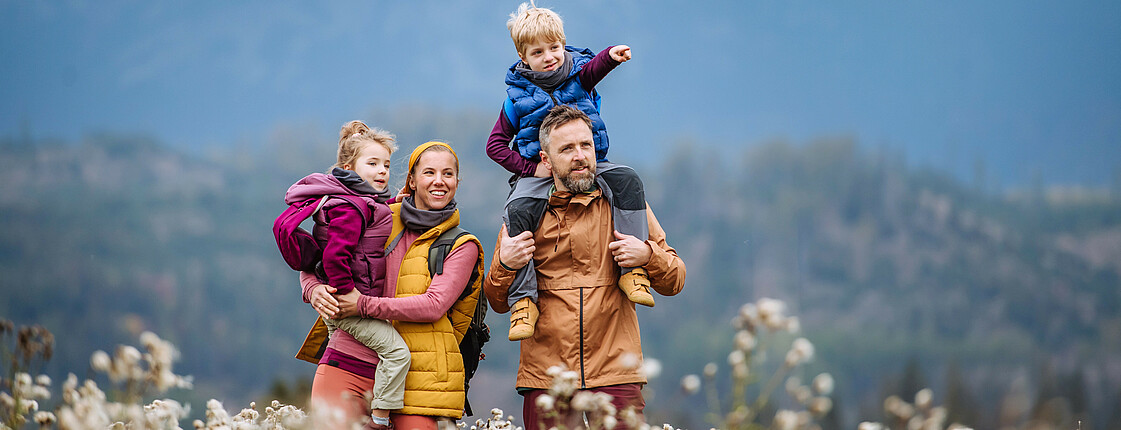 Eine Familie mit zwei Kindern in Wanderkleidung steht in einer blühenden Bergwiese.