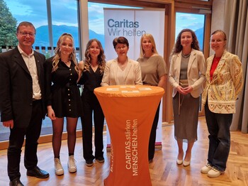 Gruppenfoto von sieben Personen, die um einen Stehtisch und vor einem Roll-Up stehen.