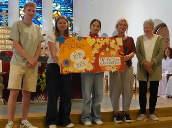 In einer Kirch präsentieren vier Jugendliche sowie eine Erwachsene einen selbst gemachten Spendenscheck in Höhe von rund 26.000 Euro.