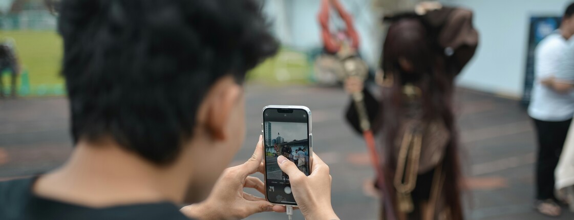 Eine Jugendlicher mit schwarzem T-Shirt fotografiert mit seinem Handy einen Cosplay-Charakter.
