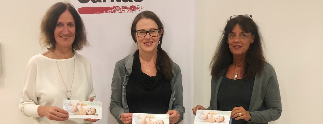 Drei Frauen vor einem Caritas Roll-Up