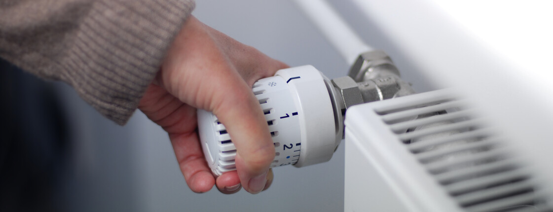 Nahaufnahme einer Hand, die an einem Heizkörper-Thermostat dreht.