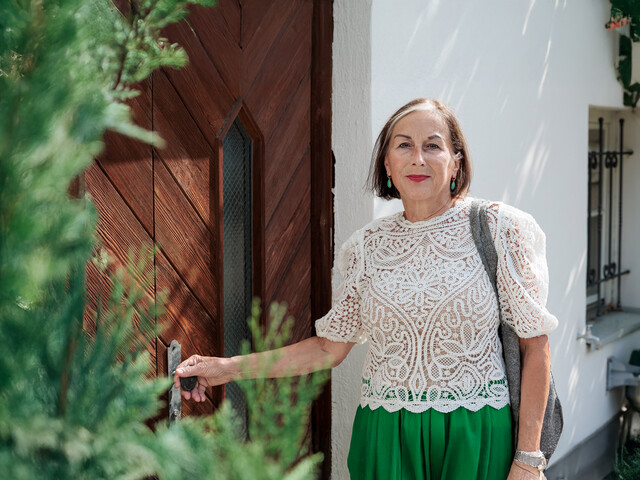 Portrait einer Haussammlerin, die an einer Eingangstüre eines traditionellen Wohnhauses in Tirol steht.