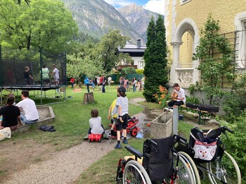 Eine große Gartenparty. Im Vordergrund stehen zwei Rollstühle.