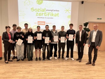Viele Personen stehen vor einer PowerPoint-Präsentation zu einem Gruppenfoto zusammen.