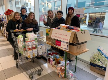 Sechs Jugendliche stehen mit zwei vollen Einkaufswägen in einem Supermartk.