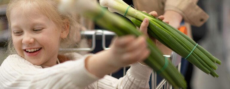 Portrait eines Jungen, der ein weißes, gestreiftes T-Shirt trägt, und sich an einem halbvollen Einkaufswagen hochhält.