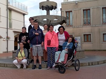 Acht Personen, darunter Menschen mit Behinderung, stehen vor einem historischen Brunnen in Caorle.