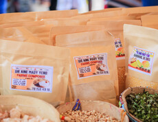 Mehrere braune Verpackungen mit Etiketten sowie Schalen mit Lebensmitteln stehen auf einem Marktstand.