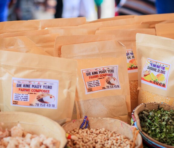 Mehrere braune Verpackungen mit Etiketten sowie Schalen mit Lebensmitteln stehen auf einem Marktstand.