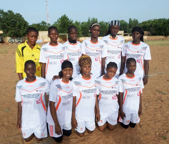 Die Sportwochen bieten Frauen die Möglichkeit, sich aus dem traditionellen Frauenbild in Mali zu befreien.  © Caritas Eine Mädchenfußballmannschaft in Mali posiert gemeinsam für ein Foto. Sie tragen weiße Trikots und stehen auf einem Sportplatz.