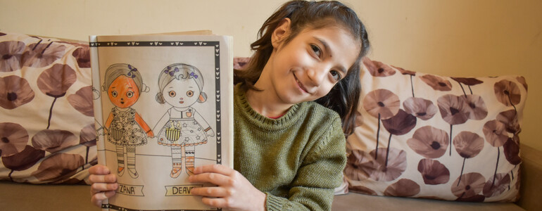 Ein Mädchen hält ein Heft mit selbstgemalten Bilder hoch.