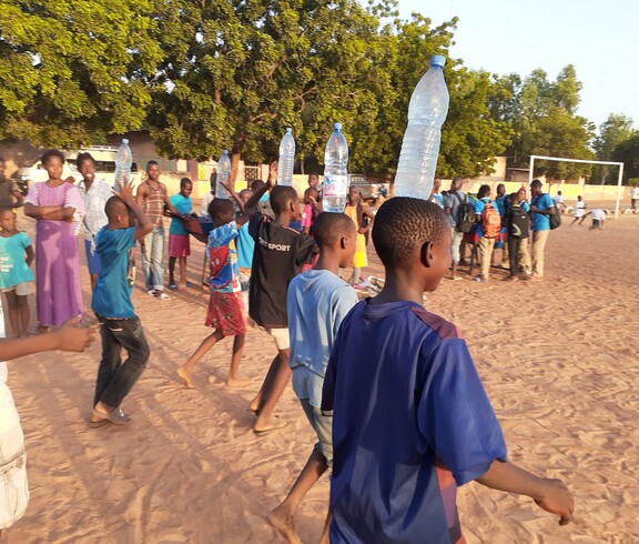 Der Flaschenlauf ist eine Variante des Eierlaufs: Die Kinder balancieren Wasserflaschen auf dem Kopf. © Caritas Mehrere Kinder nehmen an einem Wettlauf teil, bei dem sie volle Wasserflaschen auf dem Kopf balancieren.