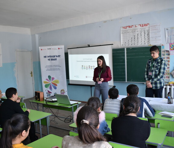 Eine Schülerinnen hält in einem Klassenzimmer eine Präsentation. Sie steht vor einer Power-Point-Präsentation.