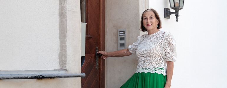 Portrait einer Haussammlerin, die an einem Hauseingang eines Gründerzeithauses steht.