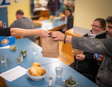 Eine Frau reicht einem Mann eine Papiertüte mit Essen über einen Tisch.