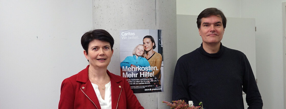 Portrait zweier Personen vor einem Kampagnenplakat.