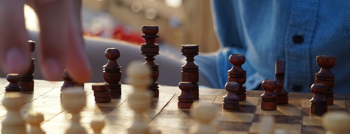 Zuhause Schach spielen Ein Mann, der ein blaues Hemd trägt, beugt sich über ein Schachbrett und macht einen Zug mit einer weißen Schachfigur.