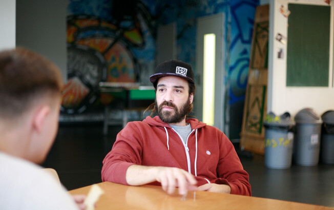 Ein Caritas-Mitarbeiter mit Hoddie und Schildkappe ist im Gespräch mit einem Jugendlichen.