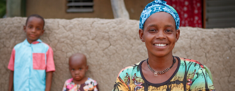 Portrait einer Frau mit zwei Kindern vor ihrem Haus in Burkina Faso.