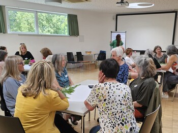 In einem großen Raum sitzen viele Personen an runden Tischen.