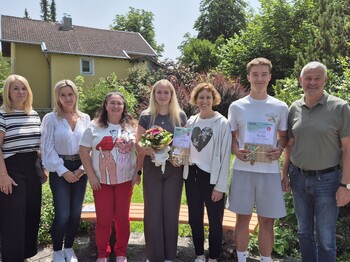 Sieben Personen stehen in einem Garten nebeneinander zu einem Gruppenfoto zusammen.