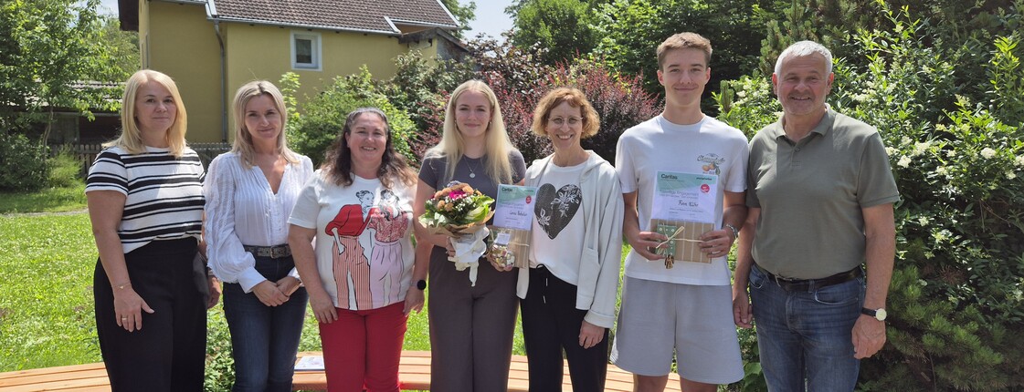 Sieben Personen stehen in einem Garten nebeneinander zu einem Gruppenfoto zusammen.
