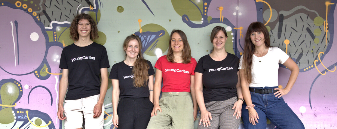 Fünf Personen stehen vor einer Wand mit bunten Graffiti zu einem Teamfoto zusammen.