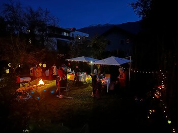 Ein festlich geschmückter Garten in der abendlichen Dunkelheit, in dem Tische und weiße Pavillons stehen.
