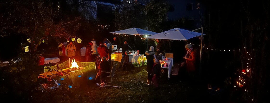 Ein festlich geschmückter Garten in der abendlichen Dunkelheit, in dem Tische und weiße Pavillons stehen.