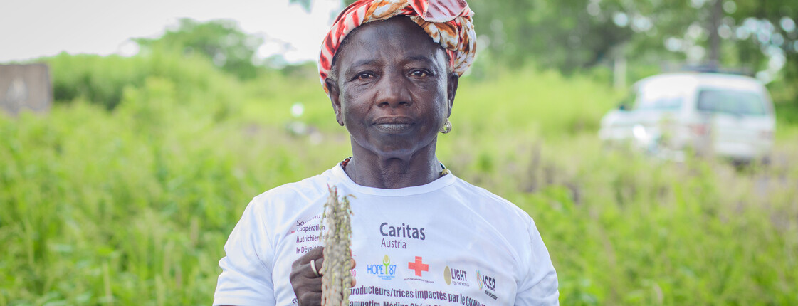 Eine Frau steht auf einem grünen Feld und hält eine Pflanze in der Hand.