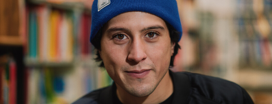 Portrait eines jungen Mannes mit schwarzer Jacke und blauer Mütze.