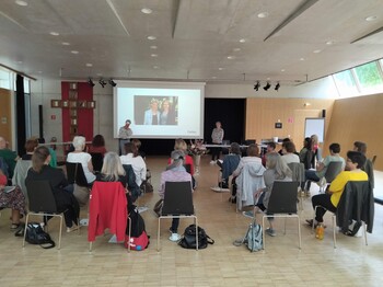 Viele Personen sitzen in einem Saal und folgen einer Präsentation.