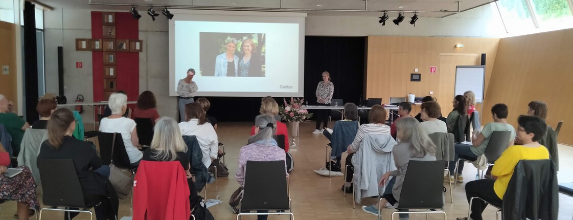 Viele Personen sitzen in einem Saal und folgen einer Präsentation.