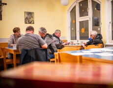 In einem Raum sitzen mehrere Personen an Tischen und spielen Karten.