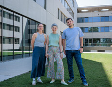 Drei Personen stehen auf einer grünen Wiese im Innenhof eines U-förmigen, modernen Gebäudes.