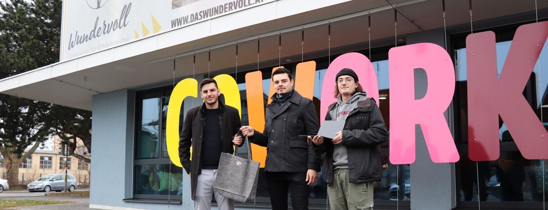 Drei Männer stehen vor einem bunten Schriftzug