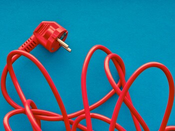 Ein verworrenes, rotes Stromkabel mit Stecker liegt auf einem blauen Hintergrund.