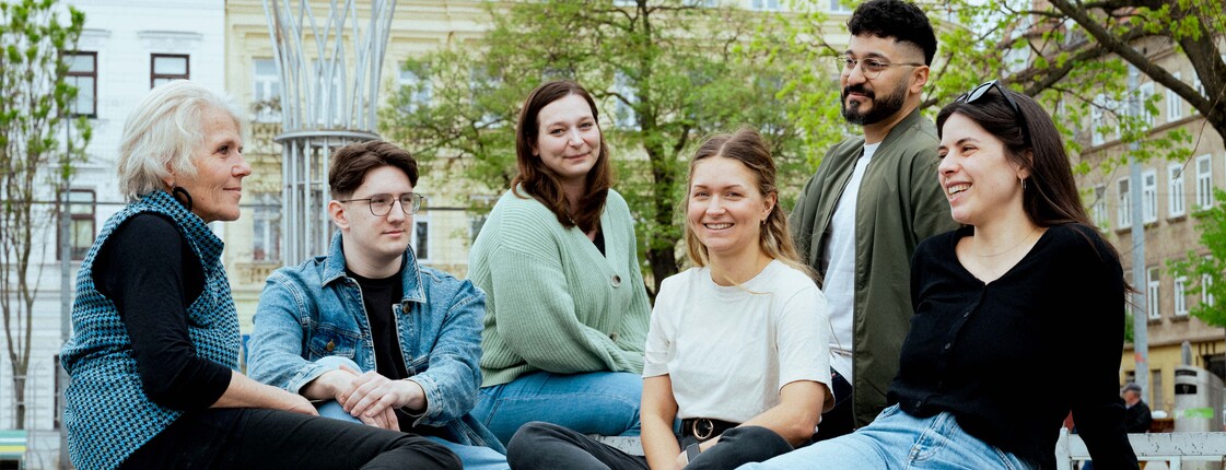 Sechs Personen, vier Frauen und zwei Männer, sitzen in einem Stadtpark.