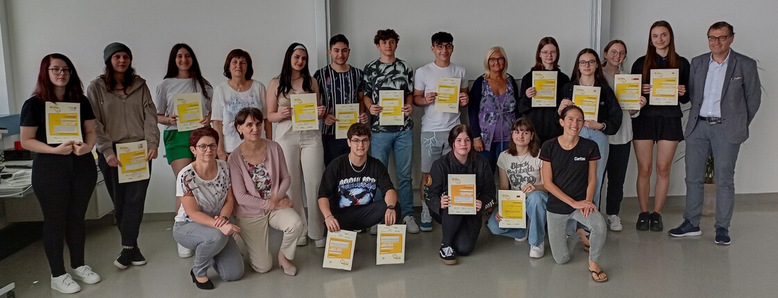 Eine Schulklasse steht für ein Gruppenfoto zusammen und hält Zertifikate hoch.