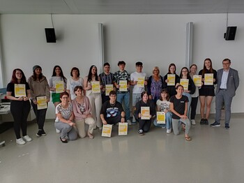 Eine Schulklasse steht für ein Gruppenfoto zusammen und hält Zertifikate hoch.