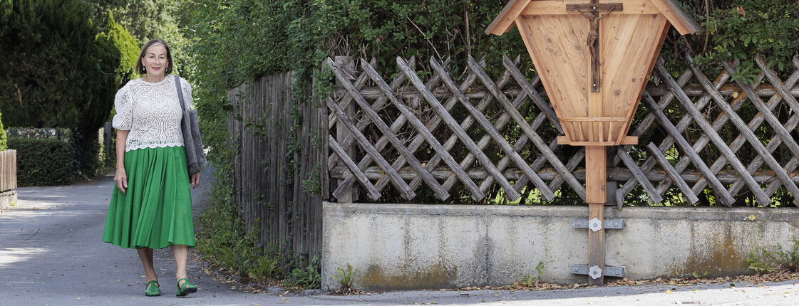 Eine Haussammlerin geht in ihrer Gemeinde an einem Kruzifix aus Holz vorbei.