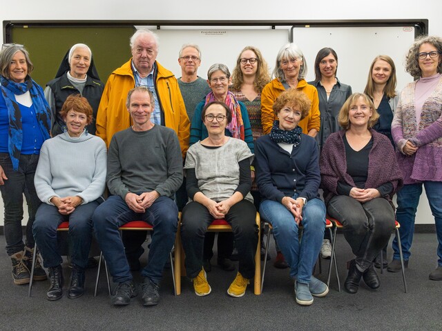 Viele Personen stehen  und sitzen in einem Seminarraum zu einem Gruppenfoto zusammen.