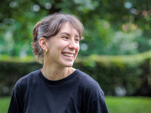 Portrait einer lachenden, jungen Frau mit schwarzem T-Shirt in einem grünen Garten.
