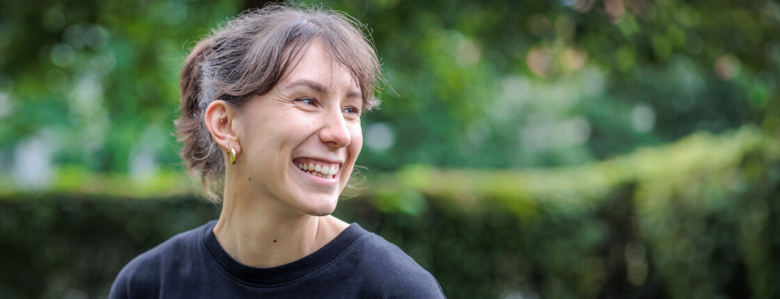 Portrait einer lachenden, jungen Frau mit schwarzem T-Shirt in einem grünen Garten.
