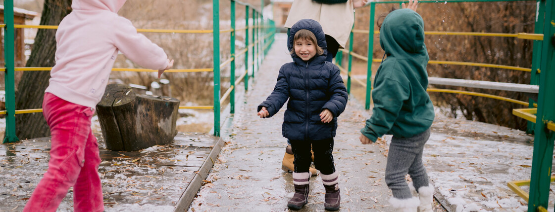 Drei Kinder spielen mit ihrer Betreuerin im Regen