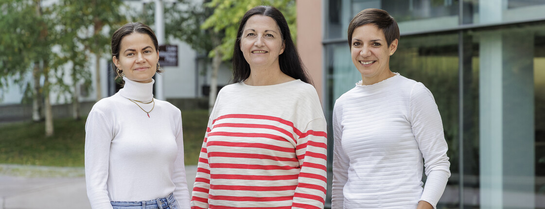 Portrait dreier Frauen in einem Innenhof mit Bäumen und modernen Bürogebäuden..