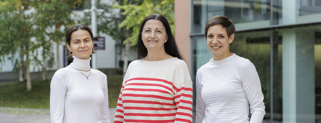 Portrait dreier Frauen in einem Innenhof mit Bäumen und modernen Bürogebäuden..