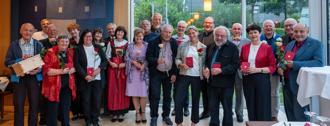 Caritas-Ehrenzeichen 2025 vergeben In einem Veranstaltungsraum mit großer Glasfassade stehen viele Personen zu einem Gruppenfoto zusammen.