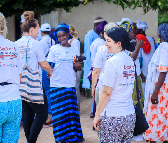 Mehrere Menschen stehen beisammen und unterhalten sich; viele tragen weiße T-Shirts mit Projektaufdruck.